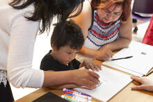 A child drawing with the guidance of two adults