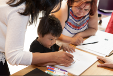 A child drawing with the guidance of two adults